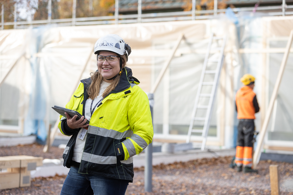 Iloinen rakennustyöntekijä työvaatteissa ja valkoinen kypärä päässä Olas Groupin uudiskohteen rakennustyömaalla.