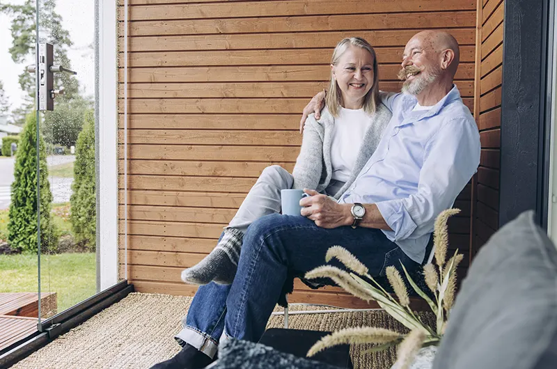 Vanhempi pariskunta istuu hymyillen terassilla miehen juodessa kahvia.